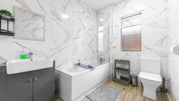 A modern bathroom with a marble wall, a bathtub, a toilet, and a sink.