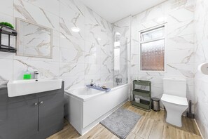A modern bathroom with a marble wall, a bathtub, a toilet, and a sink. - Modern 4BR Home|Sleep 7|Free Parking|Self check in (Southend-on-Sea)
