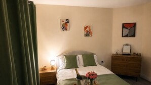 A hotel room with a bed, a nightstand, a dresser, and artwork on the walls.