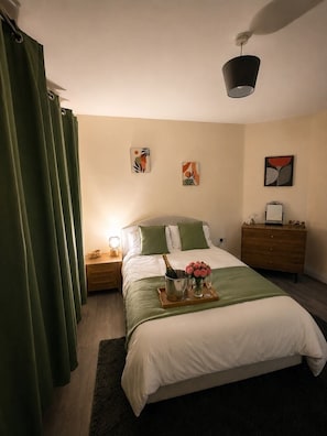 A hotel room with a bed, a nightstand, a dresser, and artwork on the walls.