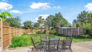 A patio with a table and chairs, surrounded by a wooden fence and greenery. - Modern 4BR Home|Sleep 7|Free Parking|Self check in (Southend-on-Sea)