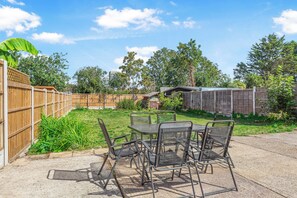 A patio with a table and chairs, surrounded by a wooden fence and greenery. - Modern 4BR Home|Sleep 7|Free Parking|Self check in (Southend-on-Sea)