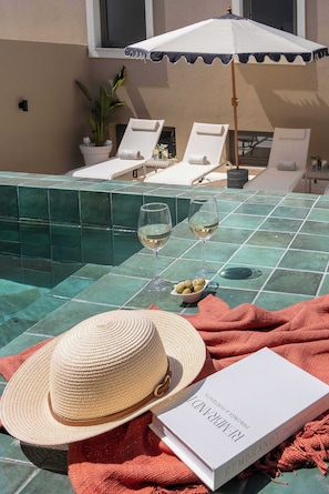 Escena junto a la piscina con sillas de descanso, un libro y un sombrero de paja.