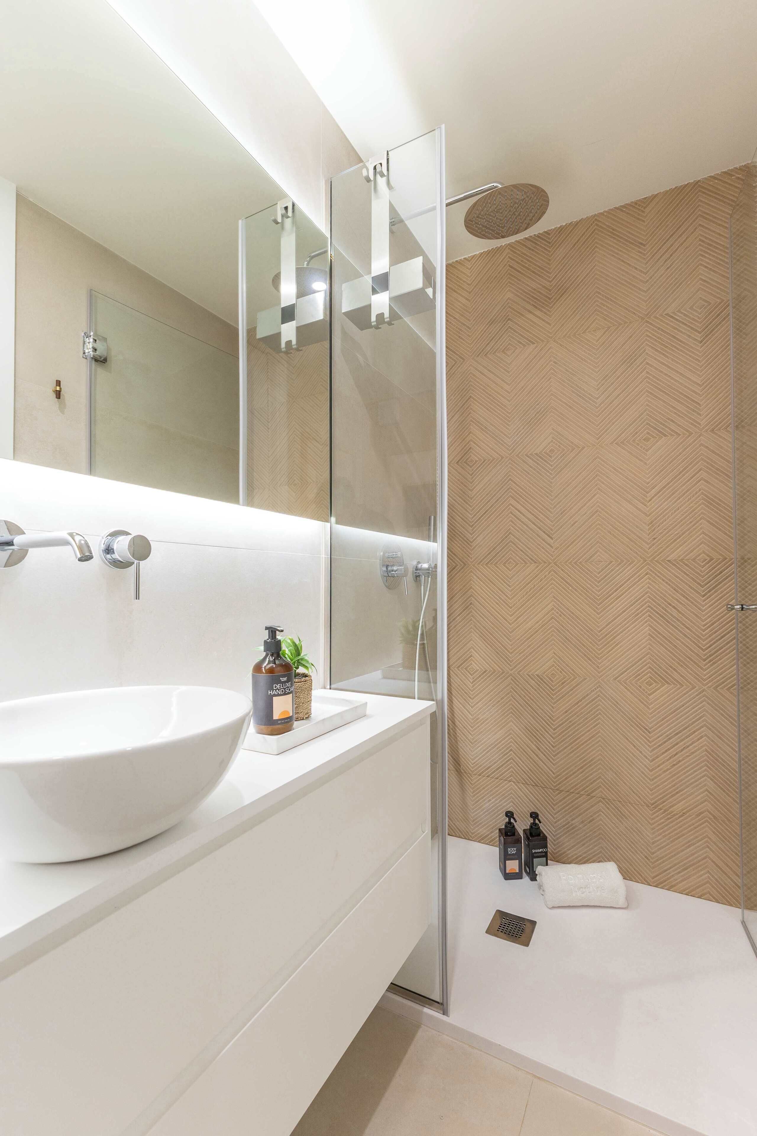 Une salle de bain moderne avec un grand lavabo blanc, une douche en verre et un mur orné d’un motif en chevrons.