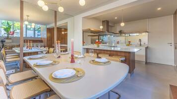 A modern dining area with a long table set for a meal, a kitchen with a central island, and a large mirror reflecting the space.