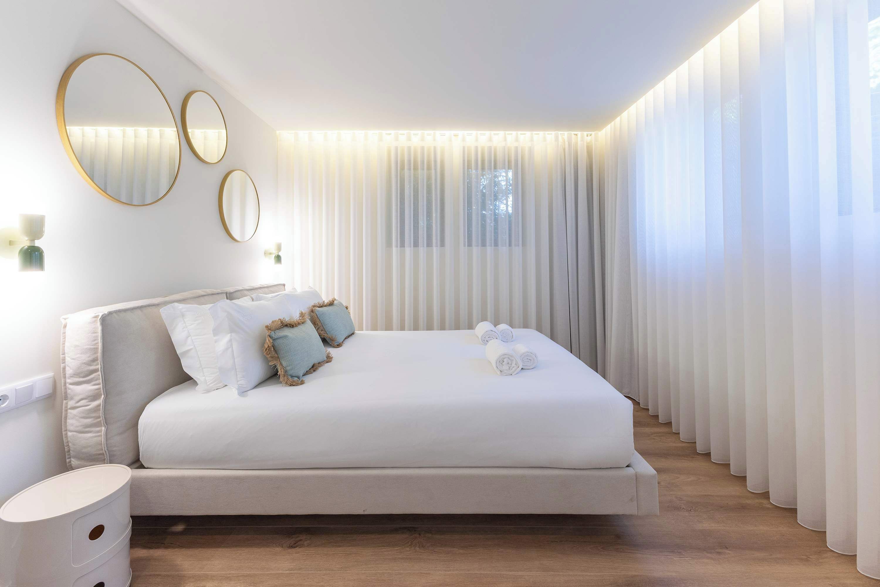 Un dormitorio moderno con una cama grande, tres espejos colocados en la pared y cortinas traslúcidas.
