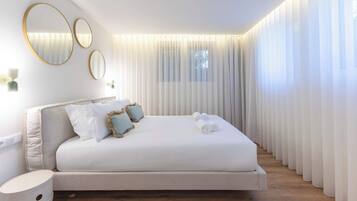 Un dormitorio moderno con una cama grande, tres espejos colocados en la pared y cortinas traslúcidas.