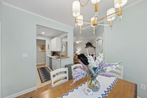 A dining area with a wooden table, white chairs, and a vase with flowers. - Blue Marlin Condo Rehoboth Beach 2BR/ 2BA (Rehoboth Beach)
