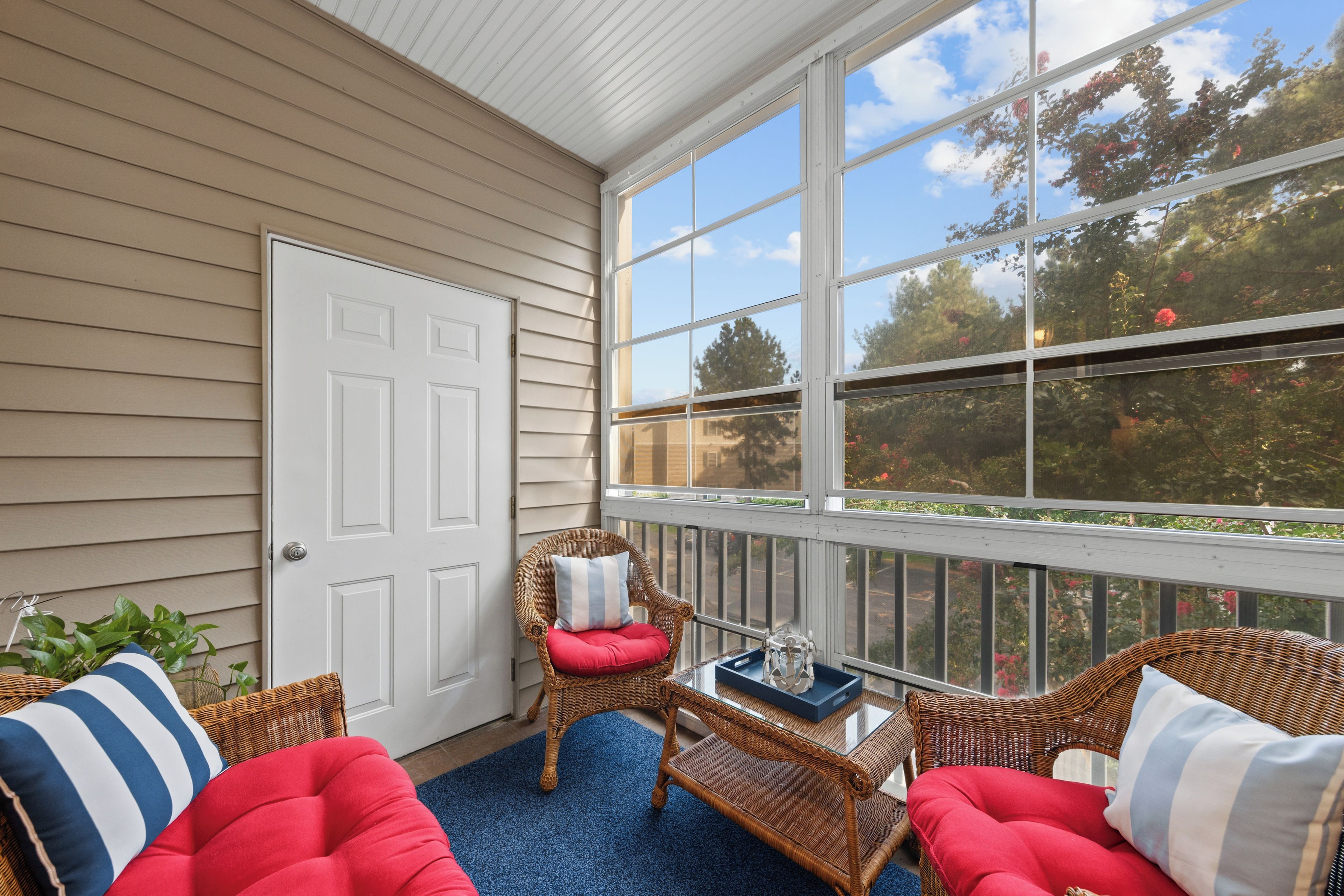 A covered porch with wicker furniture, a glass coffee table, and a view of the outdoors.