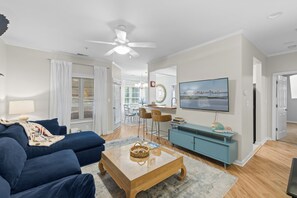 Ein modernes Wohnzimmer mit einer Couch, einem Couchtisch, einem Fernseher und einem Essbereich mit Stühlen und einem Tisch.