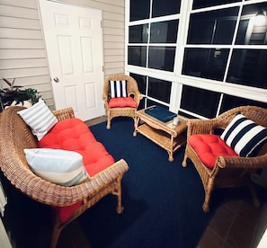 Ein Zimmer mit Rattanmöbeln, einem blauen Teppich und einem großen Fenster.