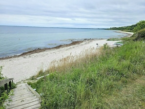 En strand med en träpromenad som leder ner till stranden, en sandstrand och ett gräsområde.