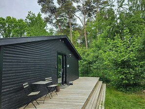 A cabin with a deck, a door, and a small outdoor seating area. - Cottage in the front row to Sejerø Bay (Fårevejle)