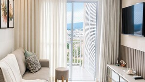 A modern hotel room with a sofa, a small table, a TV, and a balcony with a view.
