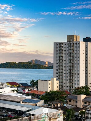 Um edifício alto com várias varandas, vista para o mar e uma ilha montanhosa ao fundo.