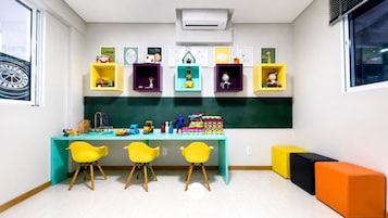 Un aula con una pizarra, estanterías llenas de juguetes infantiles y sillas amarillas.