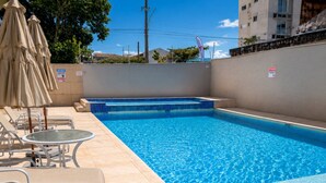 A swimming pool with steps, lounge chairs, and umbrellas.