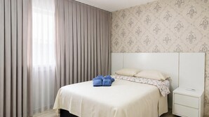 Un dormitorio con cama, cortinas, una mesita de noche y un papel tapiz floral.