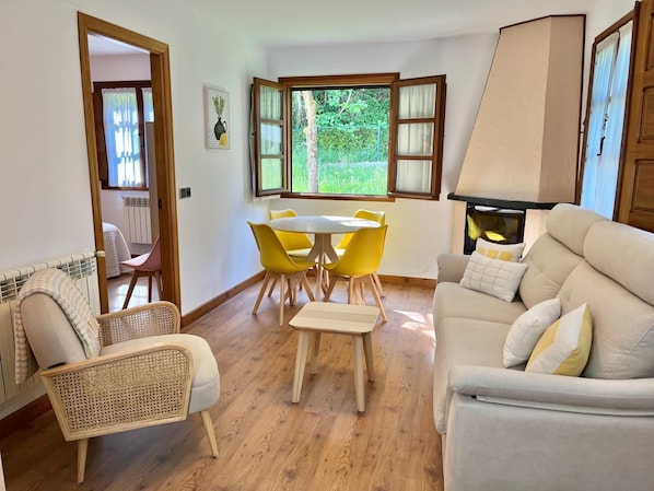 A room with a dining table, yellow chairs, a sofa, a wicker chair, and a fireplace.