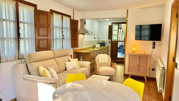 A living room with a sofa, yellow chairs, a round table, a TV, and a kitchen in the background. - BREZO APARTMENT, 10 MINUTES FROM CANGAS DEL NARCEA (Veigaipope)