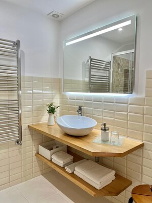 A modern bathroom with a white sink, a mirror, a towel rack, and a shelf with folded towels.