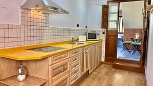 A kitchen with a yellow countertop, wooden cabinets, a microwave, and a window overlooking a patio area. - BREZO APARTMENT, 10 MINUTES FROM CANGAS DEL NARCEA (Veigaipope)