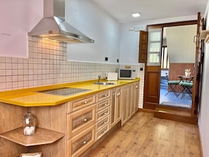 A kitchen with a yellow countertop, wooden cabinets, a microwave, and a window overlooking a patio area.