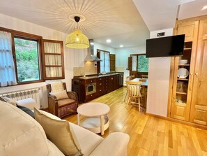 A cozy living room with a sofa, a small round table, and a kitchen area with wooden cabinets and a TV.