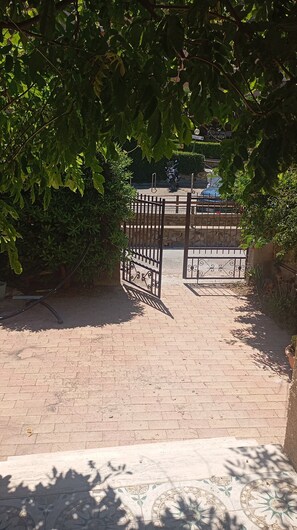 A paved pathway leading to a gated entrance, surrounded by lush greenery. - Casa Glicine Isola Del Giglio: Sea View, Private Terrace and Garden (Giglio Campese)
