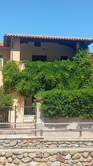 A building with a tiled roof, a stone wall, and a metal fence. - Casa Glicine Isola Del Giglio: Sea View, Private Terrace and Garden (Giglio Campese)