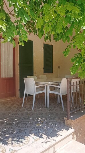An outdoor patio with a table and chairs, a patterned floor, and a wall with shutters. - Casa Glicine Isola Del Giglio: Sea View, Private Terrace and Garden (Giglio Campese)