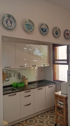 A kitchen with white cabinets, a black countertop, and a window. There are plates with designs on the wall above the cabinets. - Casa Glicine Isola Del Giglio: Sea View, Private Terrace and Garden (Giglio Campese)