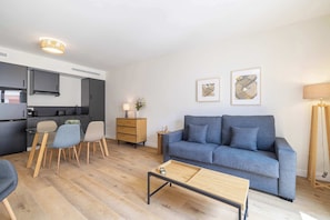 Ein modernes Wohnzimmer mit grauem Sofa, Couchtisch aus Holz und einem Essbereich mit Stühlen und einem Glastisch.