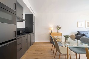 Eine moderne Küche mit Einbaugeräten, ein Essbereich mit Glastisch und ein Wohnbereich mit Sofa und Wandbildern.