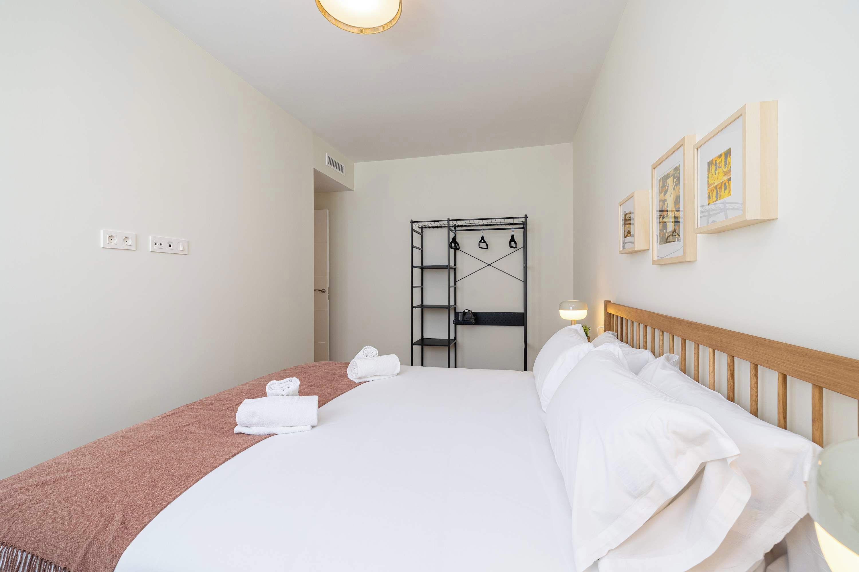 Une chambre d’hôtel comprenant un lit, une tête de lit en bois, un porte-manteau fixé au mur et une porte donnant sur une autre pièce.