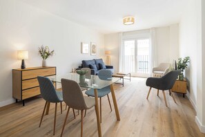 Una sala de estar moderna con una mesa de vidrio, dos sofás, una mesa de centro y una mesita de noche con una lámpara.