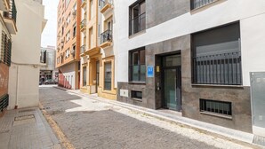 Een smalle stadstraat met meerlaagsgebouwen, een zichtbaar AT-teken en een verhard voetpad.