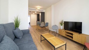 Een moderne woonkamer met een grijze bank, een houten salontafel en een tv op een houten dressoir.