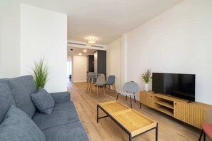 Ein modernes Wohnzimmer mit einem grauen Sofa, einem Holztisch und einem Fernseher auf einem Holzständer.