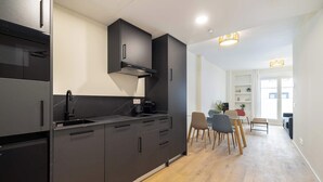 Een moderne keuken met zwarte kasten, een inbouwoven en een eethoek met een tafel en stoelen.