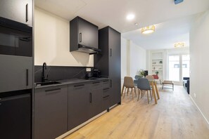 Eine moderne Küche mit schwarzen Schränken, einem Einbauofen und einem Essbereich mit Tisch und Stühlen.