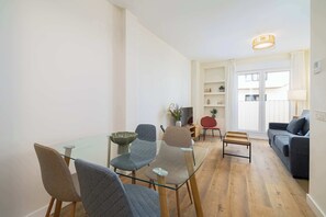 Ein modernes Wohnzimmer mit einem Glastisch, grauen Polsterstühlen, einem grauen Sofa und Holzboden.