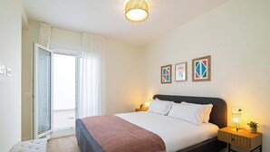 Een slaapkamer met een bed, nachtkastje, lamp en een uitzicht door een deur.