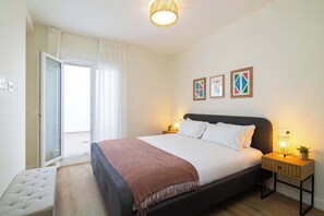 Ein Schlafzimmer mit Bett, Nachttisch, Lampe und Blick durch eine Tür.