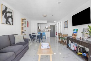 Ein modernes Wohnzimmer mit einem grauen Sofa, einem Holztisch und einer Essecke mit blauen Stühlen.