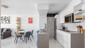 Una cocina moderna con armarios blancos, microondas integrado y refrigerador de acero inoxidable.