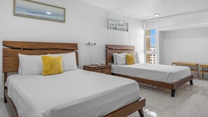 Habitación de hotel con dos camas, una mesita de noche, una pequeña mesa y una ventana con vista a edificios.