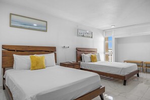 Ein Hotelzimmer mit zwei Betten, einem Nachttisch, einem kleinen Tisch und einem Fenster mit Blick auf Gebäude.
