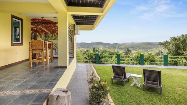 A covered outdoor area with a view of hills, a wooden bench, a table, and a chair. - The Ceiba Villa by Otium (Aguas Claras)