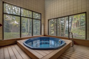 A hot tub in a corner with large windows, wooden flooring, and a view of trees and a building. - Spacious Mountain Retreat with Private Balcony (Keystone)